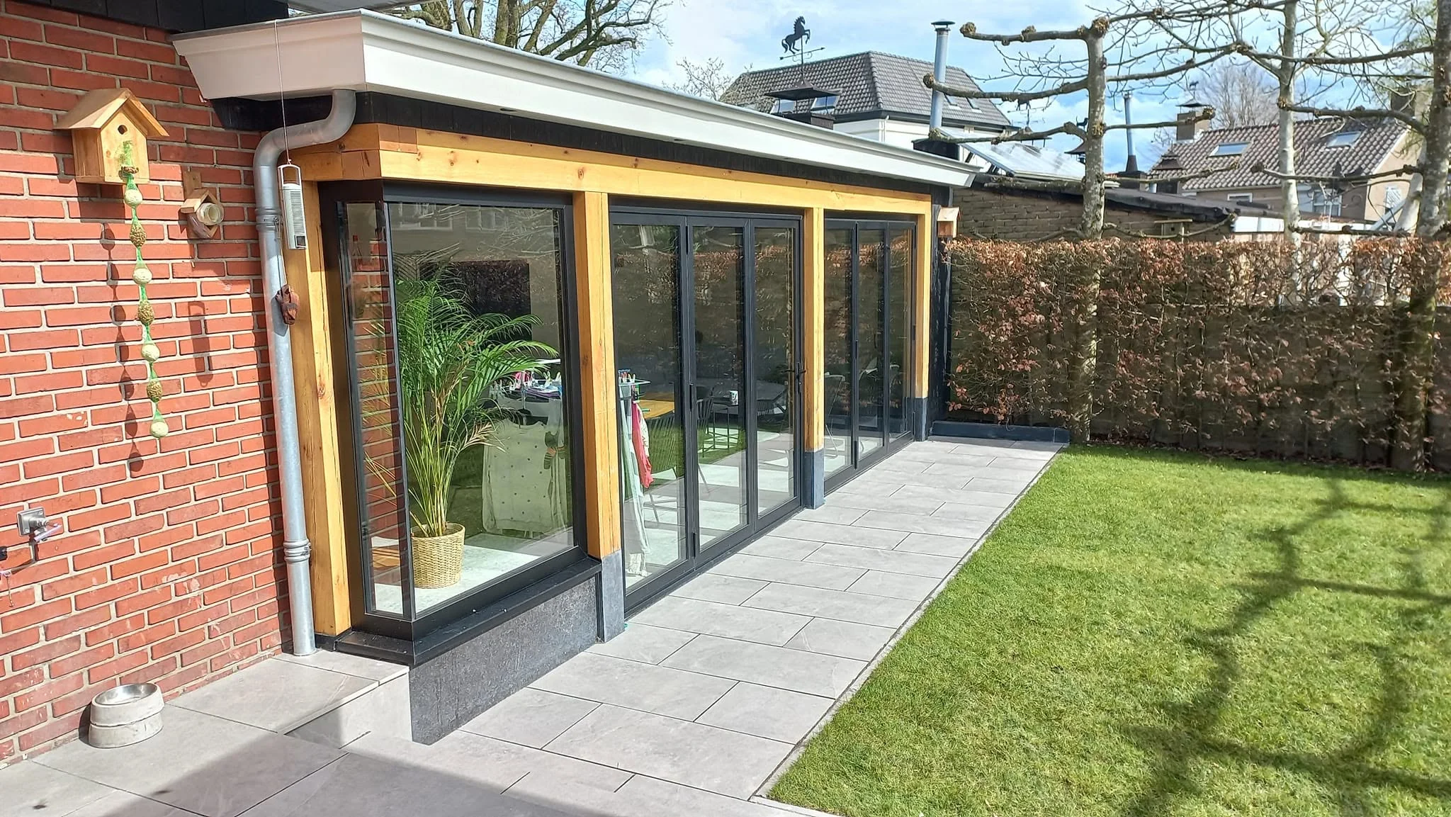 Houten aanbouw met zwarte glazen pui en terras aan de tuin