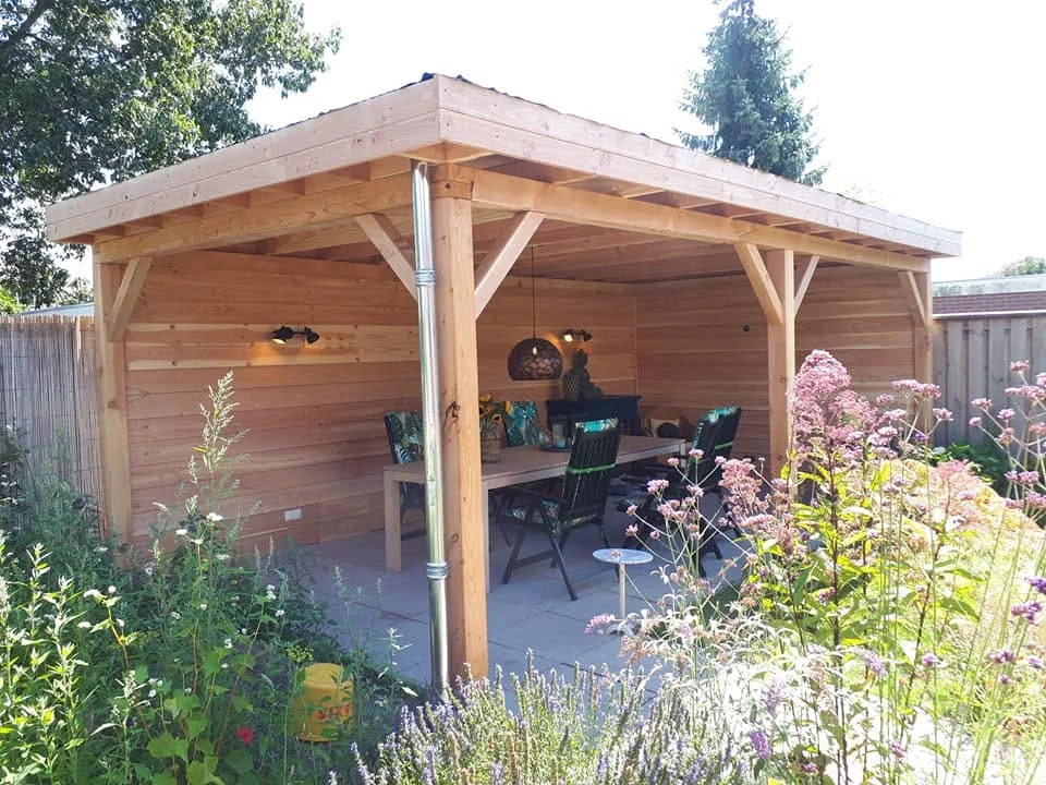 Houten overkapping met zitplek tussen bloeiende tuinbeplanting