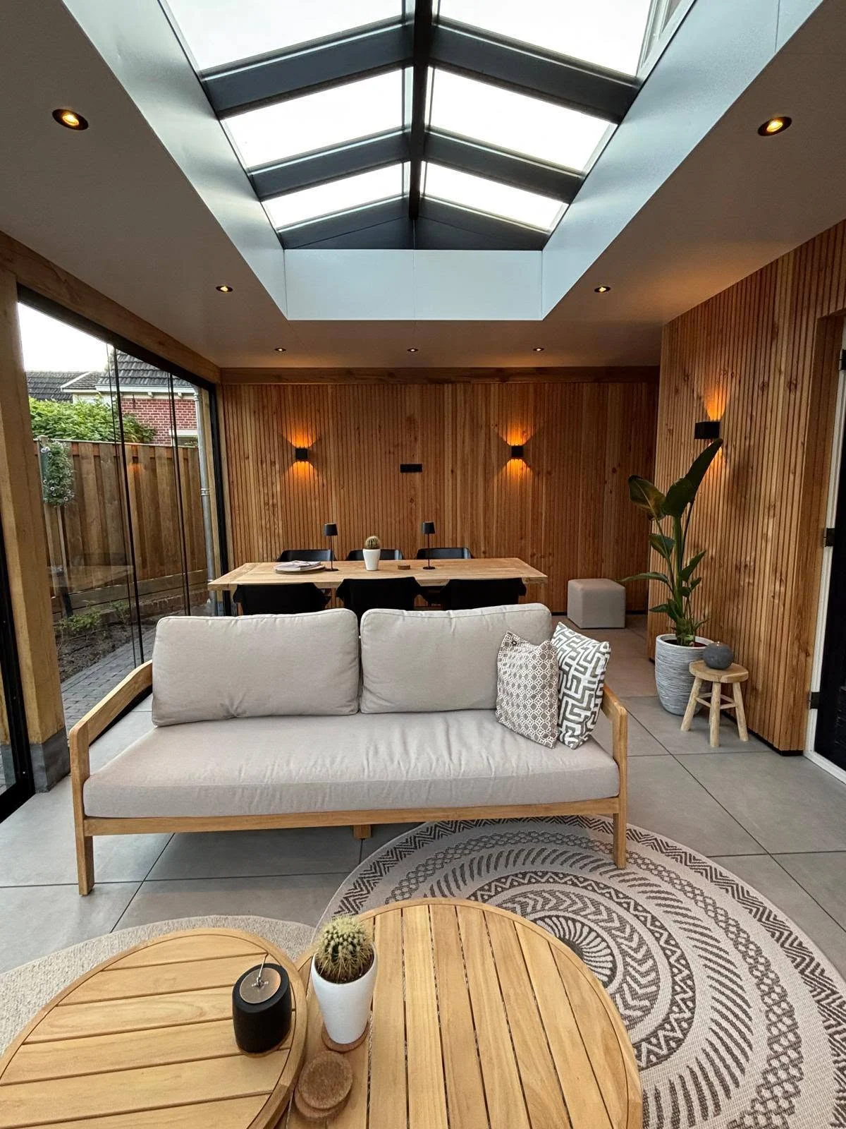 Interieur van een veranda met houten wandafwerking, glazen dak en loungehoek