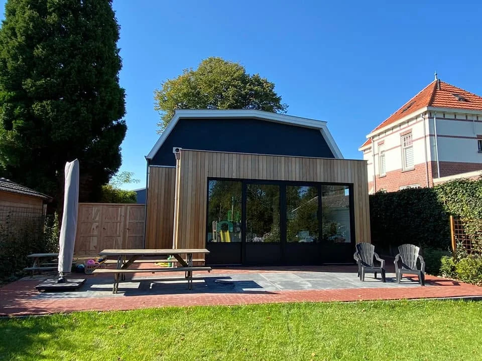 Tuinhuis met houten gevelbekleding en zwarte topgevel aan een terras