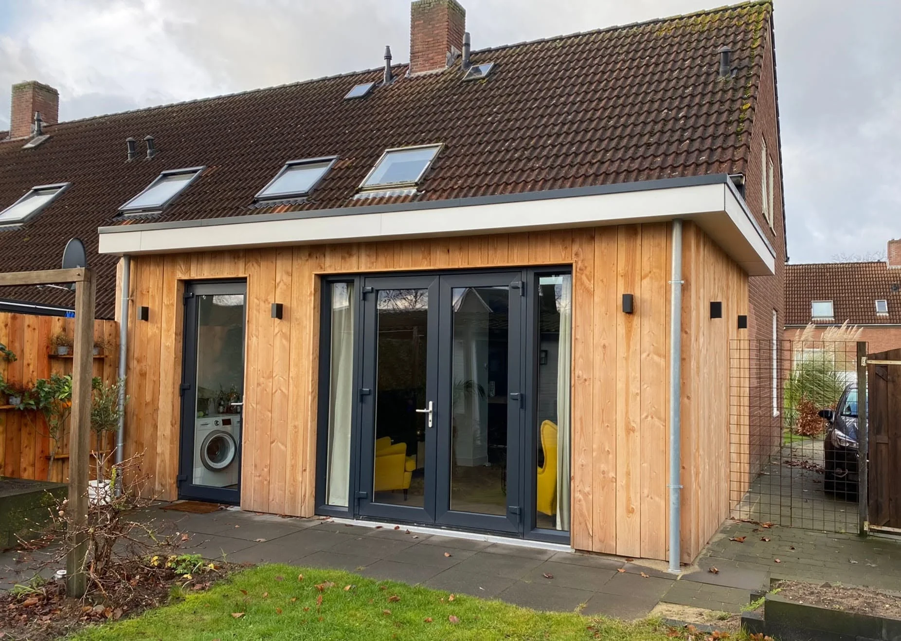 Uitbouw met houten gevelbekleding en donkere kozijnen